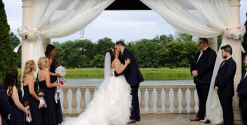 A bride and groom share their first kiss under a white-draped gazebo overlooking the lake at Blue Sky Vineyard.