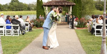 A newlywed couple shares their first kiss at the outdoor ceremony pavilion at Blue Sky Vineyard surrounded by guests.