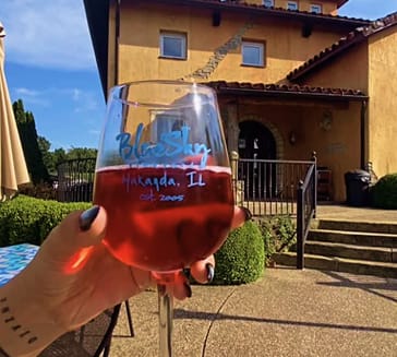 Glass of rosé wine held in front of Blue Sky Vineyard’s Tuscan-style building.
